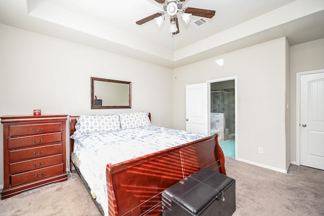 bedroom with a raised ceiling, ceiling fan, light colored carpet, and connected bathroom