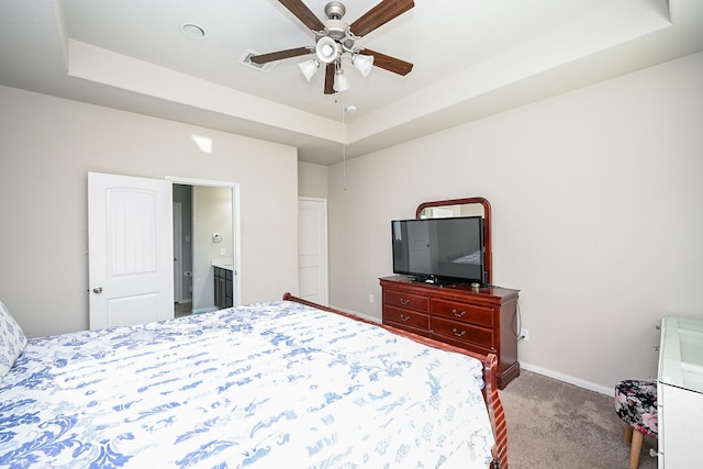 carpeted bedroom with a tray ceiling, connected bathroom, and ceiling fan