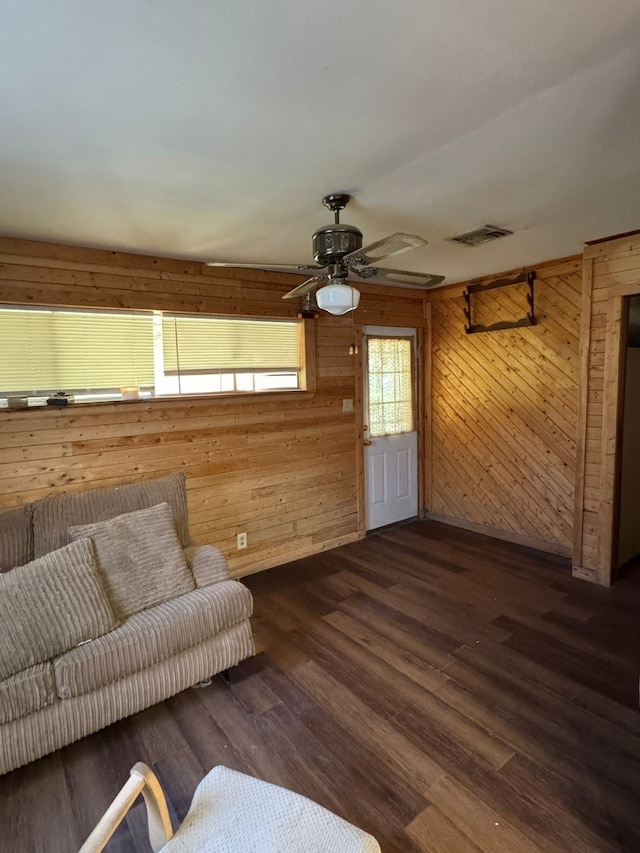 unfurnished living room with ceiling fan, wood walls, and dark hardwood / wood-style flooring