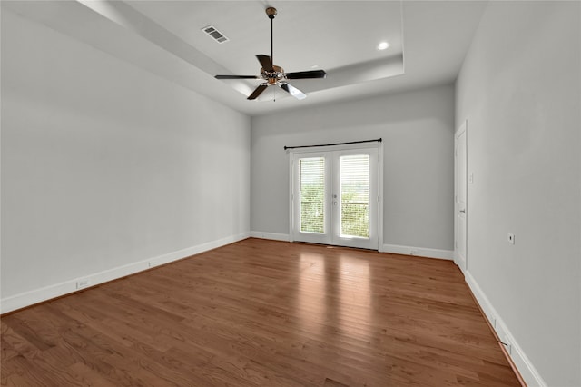 empty room featuring hardwood / wood-style floors, ceiling fan, and a tray ceiling