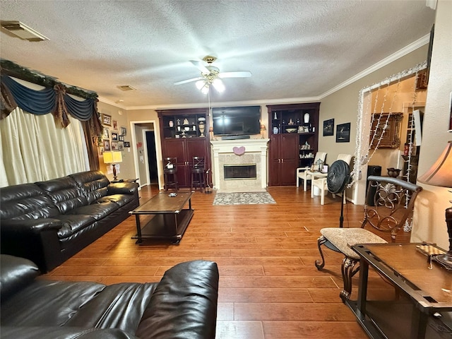 living room featuring ceiling fan, wood-type flooring, a textured ceiling, and ornamental molding