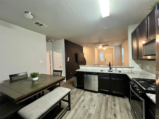 kitchen featuring sink, ceiling fan, light stone countertops, appliances with stainless steel finishes, and light hardwood / wood-style floors