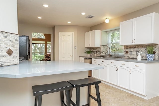 kitchen featuring tasteful backsplash, kitchen peninsula, fridge, a kitchen bar, and white cabinets