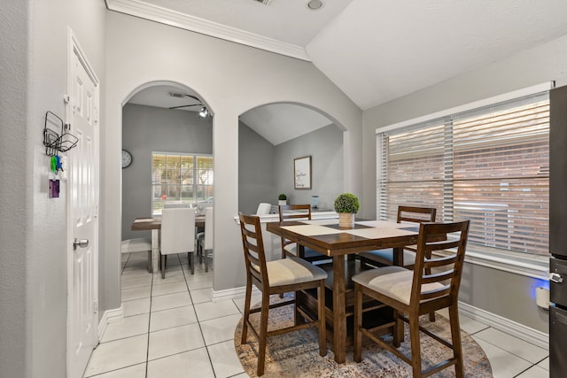 tiled dining room featuring ceiling fan, ornamental molding, and vaulted ceiling