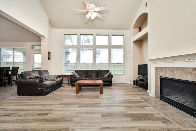 living room with a tiled fireplace, vaulted ceiling, ceiling fan, and light hardwood / wood-style flooring