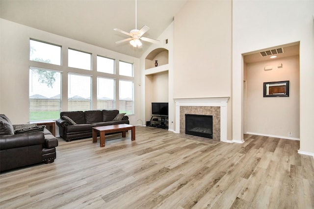 living room featuring a tiled fireplace, a towering ceiling, ceiling fan, and light hardwood / wood-style flooring