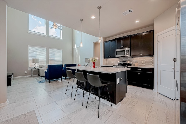 kitchen featuring decorative backsplash, appliances with stainless steel finishes, ceiling fan, pendant lighting, and a center island