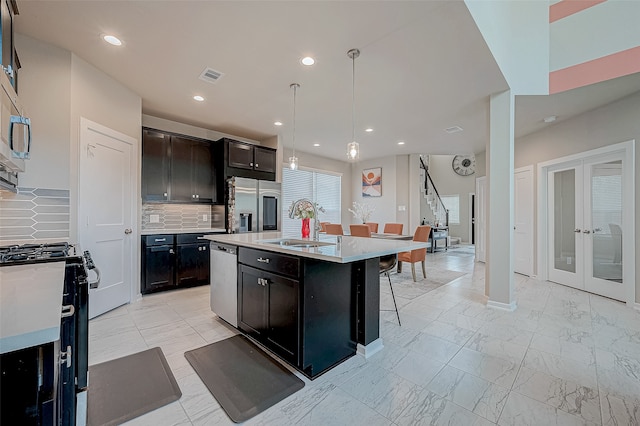 kitchen with appliances with stainless steel finishes, backsplash, a kitchen breakfast bar, pendant lighting, and an island with sink