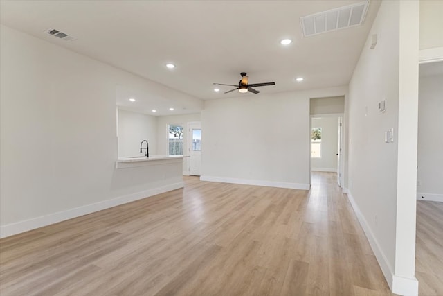 unfurnished living room featuring ceiling fan, sink, a healthy amount of sunlight, and light wood-type flooring