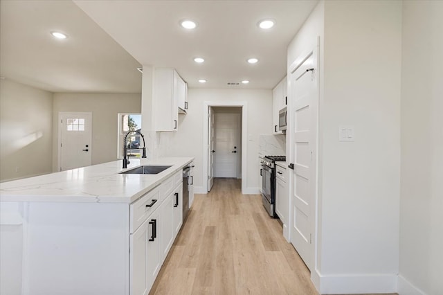 kitchen featuring light stone countertops, appliances with stainless steel finishes, light wood-type flooring, sink, and white cabinetry