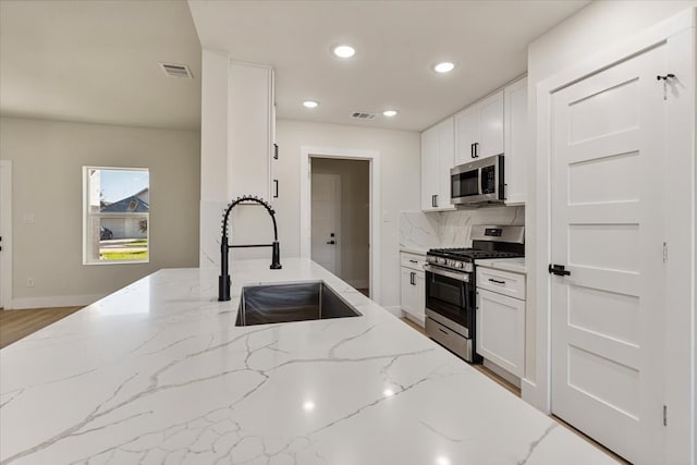 kitchen with sink, white cabinets, light stone counters, and stainless steel appliances