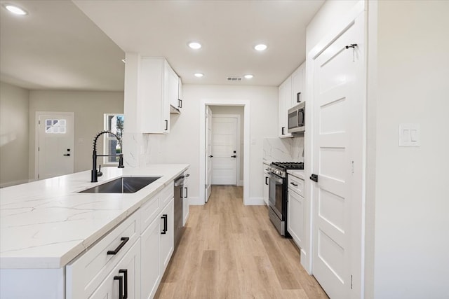 kitchen featuring sink, tasteful backsplash, light hardwood / wood-style flooring, white cabinets, and appliances with stainless steel finishes