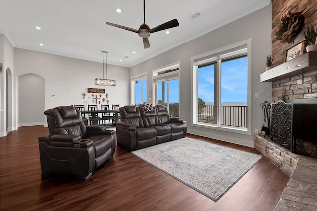 living room featuring dark hardwood / wood-style floors, ceiling fan, crown molding, and a fireplace