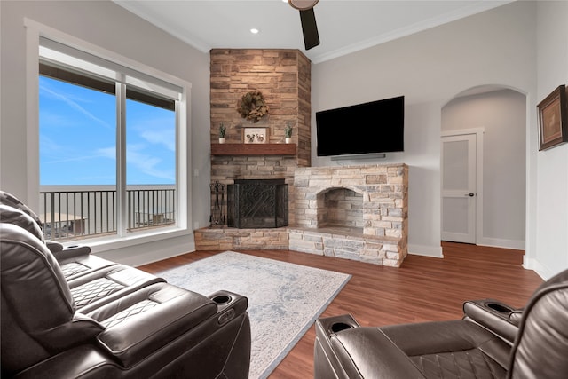 living room featuring dark hardwood / wood-style floors, a stone fireplace, ceiling fan, and crown molding