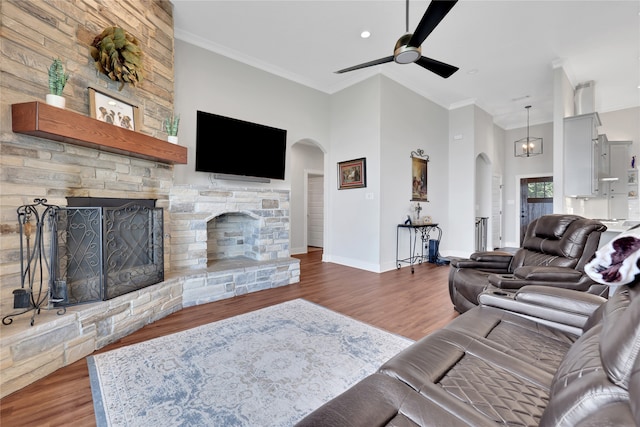 living room with dark hardwood / wood-style flooring, a towering ceiling, a fireplace, ceiling fan with notable chandelier, and ornamental molding