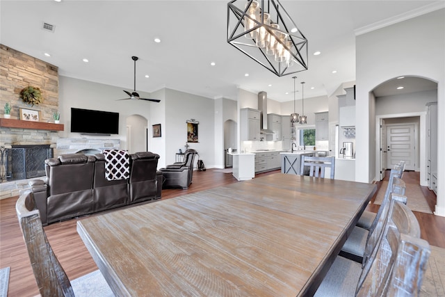 dining room featuring ceiling fan with notable chandelier, a stone fireplace, ornamental molding, and light hardwood / wood-style flooring