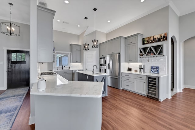 kitchen featuring beverage cooler, dark hardwood / wood-style floors, pendant lighting, a center island with sink, and appliances with stainless steel finishes