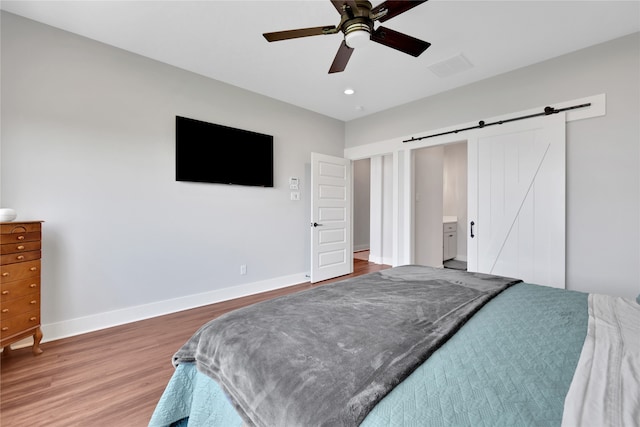 bedroom with ceiling fan, a barn door, wood-type flooring, and connected bathroom