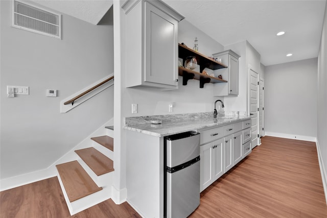 kitchen with light stone countertops, stainless steel fridge, light hardwood / wood-style floors, and a textured ceiling