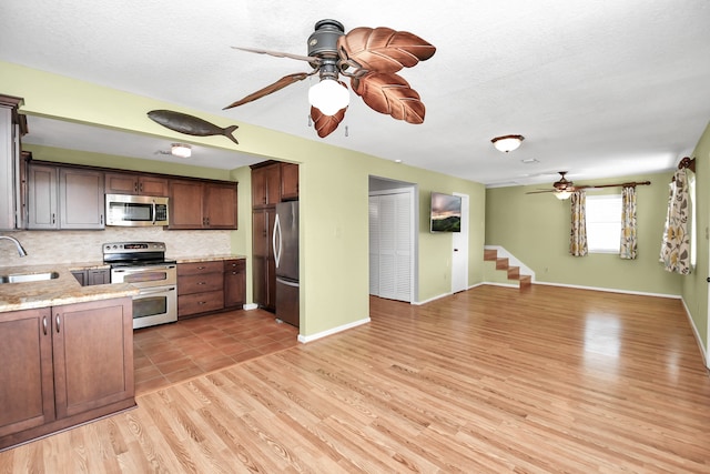 kitchen with dark brown cabinetry, sink, stainless steel appliances, tasteful backsplash, and light hardwood / wood-style flooring