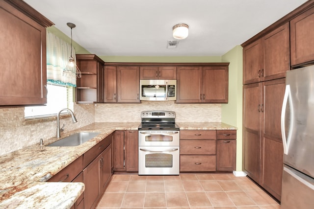 kitchen with light stone countertops, sink, hanging light fixtures, light tile patterned flooring, and appliances with stainless steel finishes