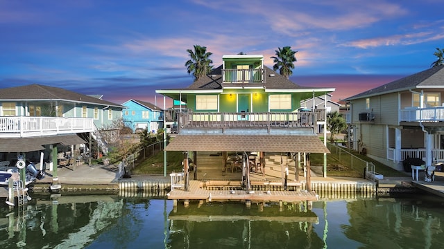 back house at dusk featuring a balcony and a deck with water view