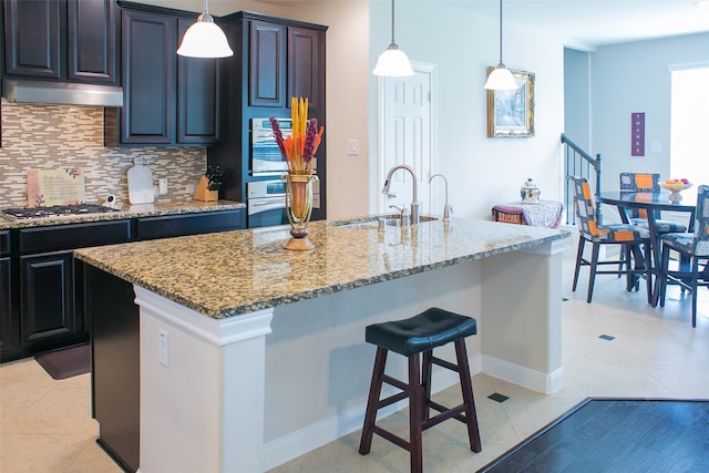 kitchen featuring light stone countertops, appliances with stainless steel finishes, tasteful backsplash, a kitchen island with sink, and sink