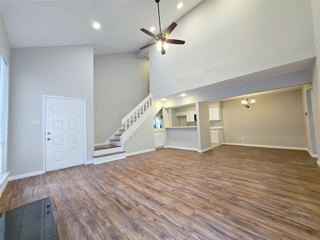 unfurnished living room with ceiling fan with notable chandelier, dark hardwood / wood-style floors, and high vaulted ceiling