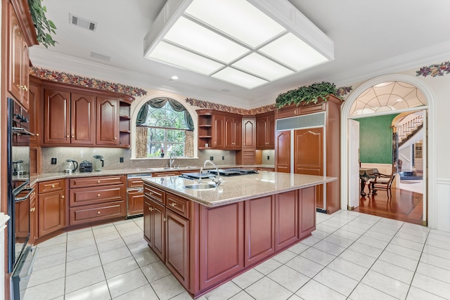 kitchen featuring a center island with sink, light stone counters, ornamental molding, and sink