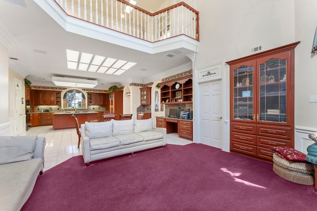 carpeted living room featuring a high ceiling, built in desk, and ornamental molding