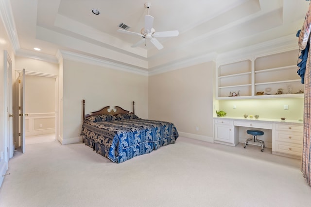 bedroom with ceiling fan, a tray ceiling, light carpet, built in desk, and ornamental molding