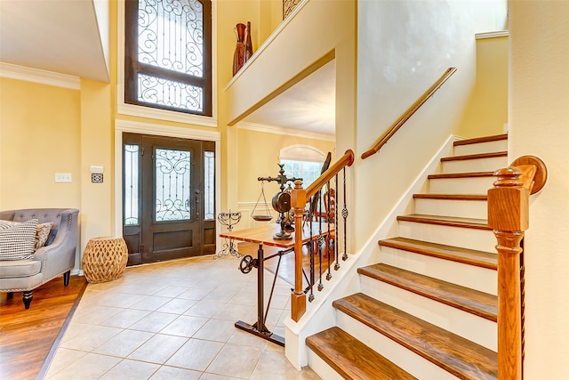 foyer with ornamental molding, a towering ceiling, a healthy amount of sunlight, and light wood-type flooring