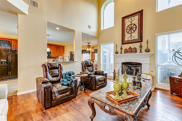 living room with a towering ceiling, hardwood / wood-style flooring, and ceiling fan