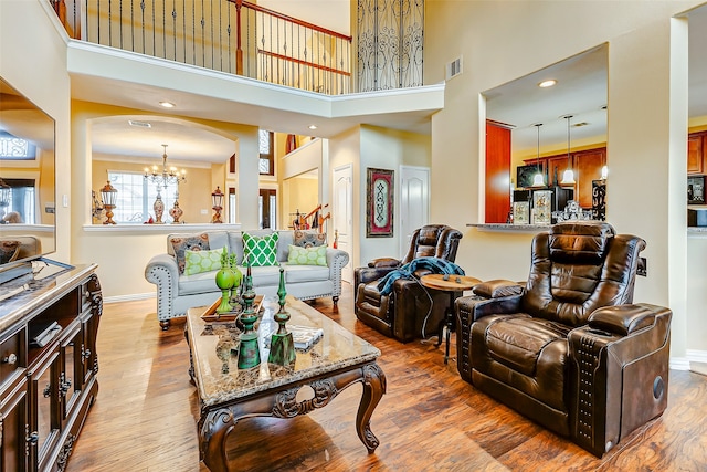 living room with a chandelier, wood-type flooring, a high ceiling, and ornamental molding