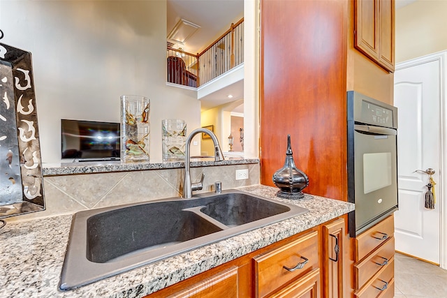 kitchen with light stone countertops, light tile patterned floors, oven, and sink