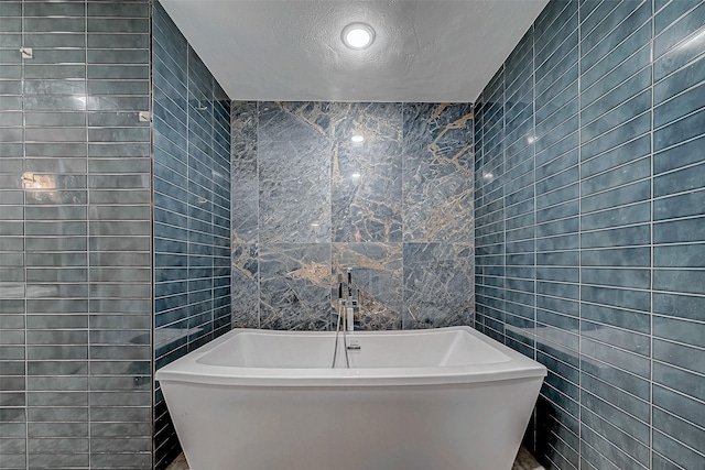 bathroom featuring a textured ceiling, a bathtub, and tile walls