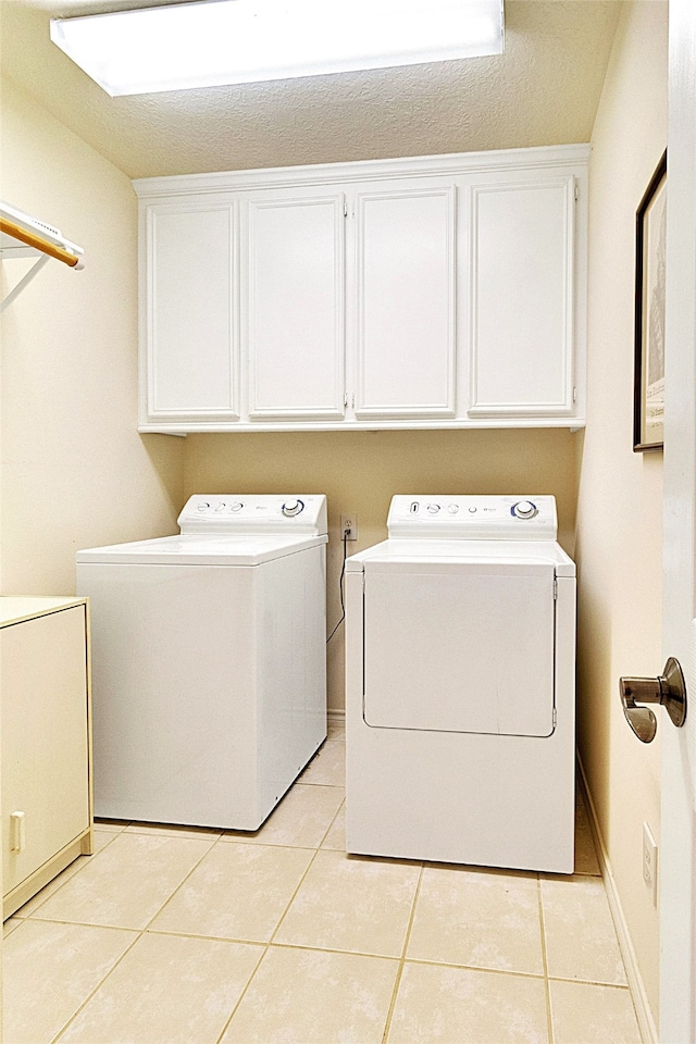 laundry room with cabinets, light tile patterned floors, washer and dryer, and a textured ceiling