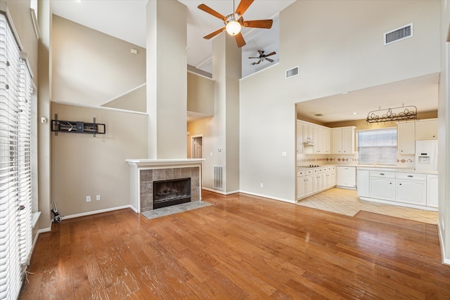 unfurnished living room with a healthy amount of sunlight, light wood-type flooring, high vaulted ceiling, and a tiled fireplace