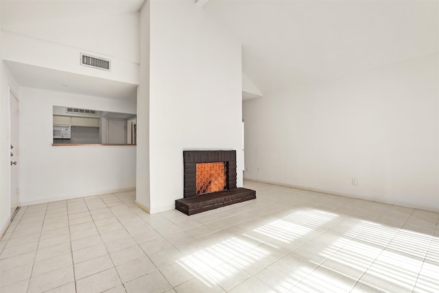 unfurnished living room with light tile patterned floors, high vaulted ceiling, and a brick fireplace