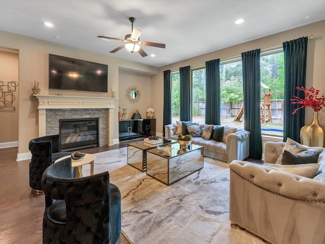 living room with a stone fireplace, ceiling fan, plenty of natural light, and light hardwood / wood-style flooring