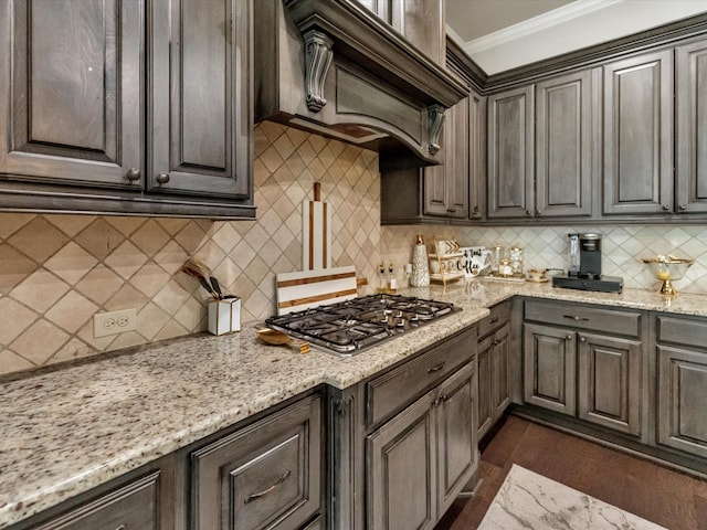 kitchen with backsplash, light stone countertops, ornamental molding, dark hardwood / wood-style flooring, and stainless steel gas cooktop