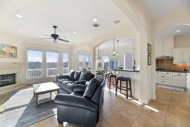 tiled living room with ceiling fan with notable chandelier and ornamental molding