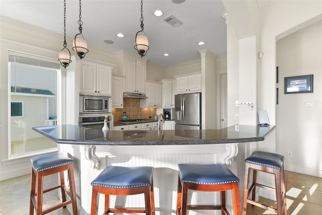 kitchen with white cabinets, a kitchen breakfast bar, ornamental molding, appliances with stainless steel finishes, and tasteful backsplash