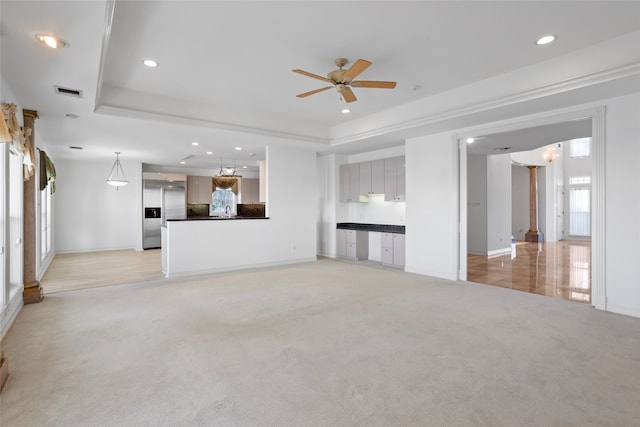 unfurnished living room featuring a raised ceiling, ceiling fan, and light colored carpet