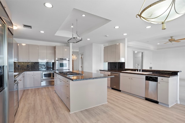 kitchen featuring a center island, hanging light fixtures, a tray ceiling, appliances with stainless steel finishes, and light wood-type flooring