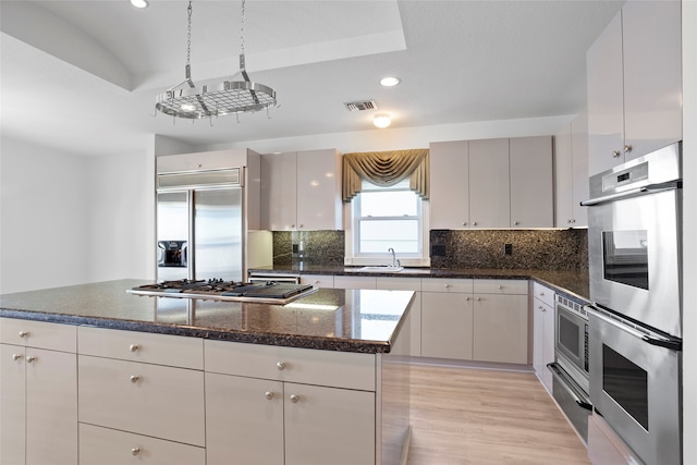 kitchen featuring stainless steel appliances, white cabinets, light hardwood / wood-style floors, decorative backsplash, and a kitchen island