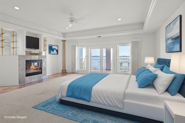 bedroom with a tray ceiling, ceiling fan, and a tiled fireplace