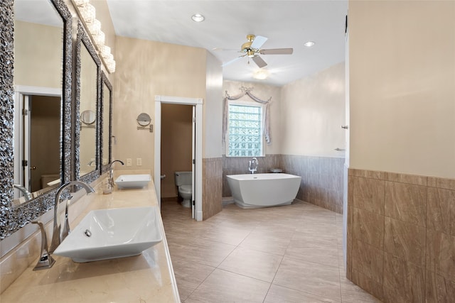 bathroom featuring tile patterned floors, ceiling fan, tile walls, toilet, and a tub