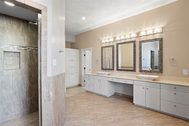 bathroom with a tile shower, vanity, and tile walls