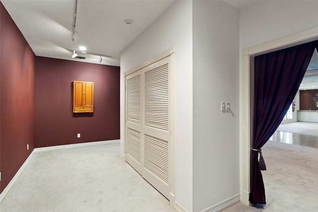 hall featuring track lighting and light colored carpet